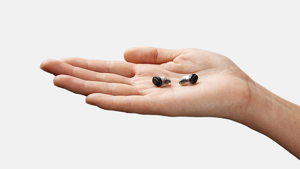 Hand holding two IIC Oticon Own hearing aids in palm