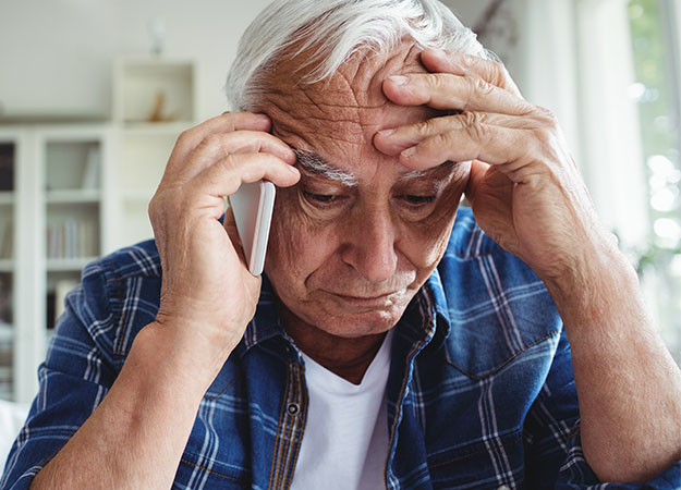 Image shows man talking on the phone while holding his head